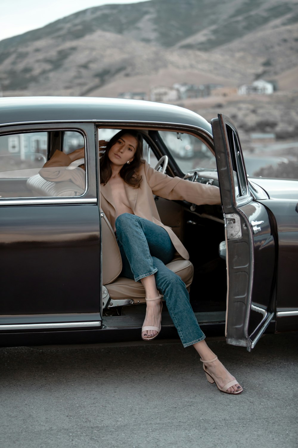 woman in blue denim jeans and brown jacket sitting on black car