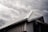 A modern building's roof with a sloped, triangular metal design is captured under a moody, overcast sky. The metallic surface of the roof contrasts with the dark, cloudy background, highlighting its architectural features.