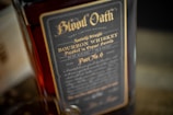 A close-up view of a bourbon whiskey bottle labeled 'Blood Oath'. The label is dark with elegant gold lettering detailing Kentucky straight bourbon whiskey finished in cognac barrels. It indicates details like 'very limited release' and '49.3% ALC/VOL'.