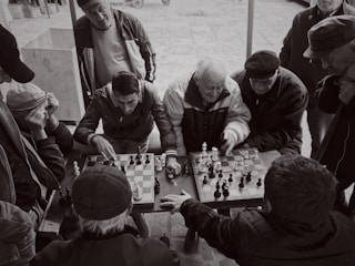 A diverse group of people gathered around a chess table, engaged in a match under soft lighting.