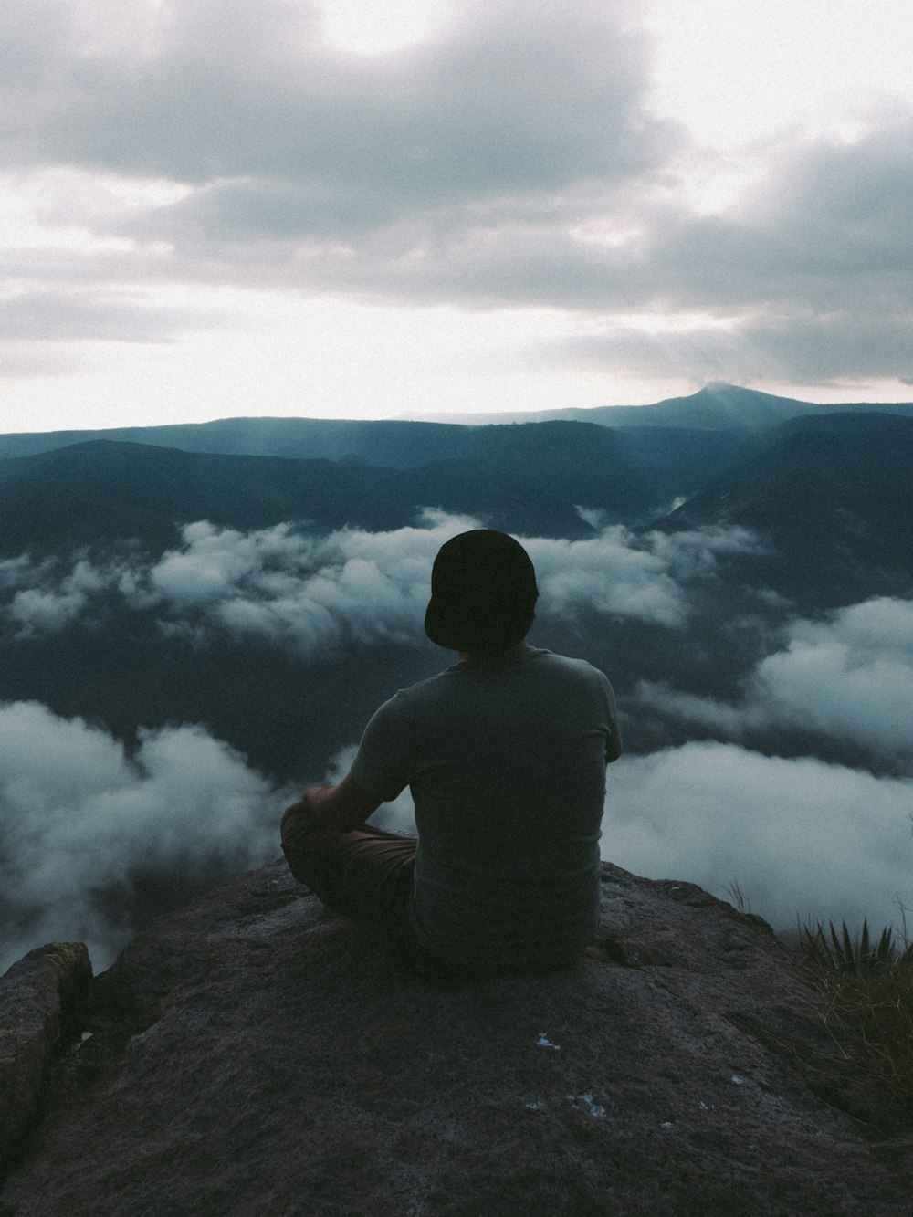 man in gray hoodie sitting on rock near lake during daytime