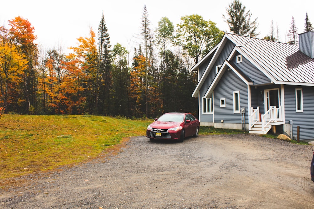 red car parked beside white wooden house