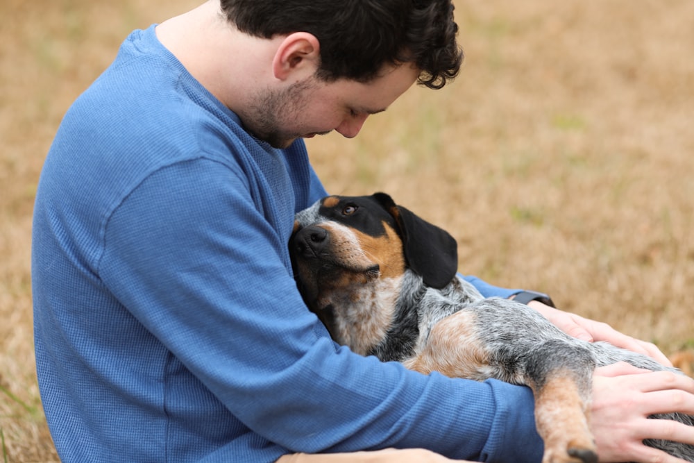 man in blue shirt hugging black and white short coated dog