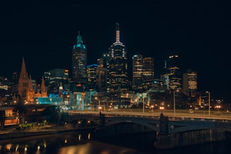 A vibrant cityscape at night with colorful lights reflecting off a calm river, inviting urban adventures.