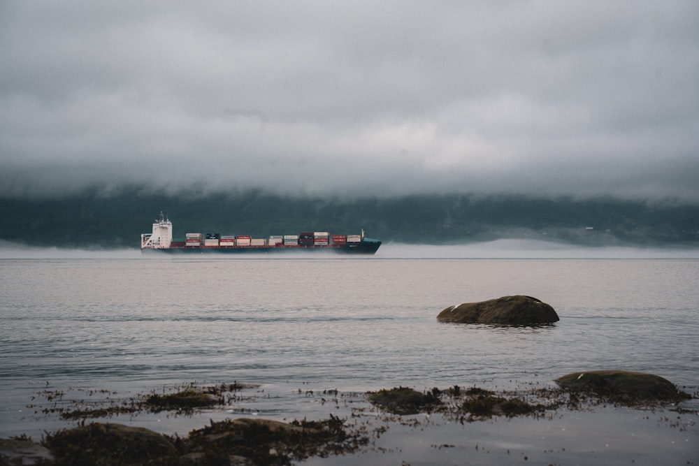 昼間、白い雲の下の海上に浮かぶ赤い貨物船
