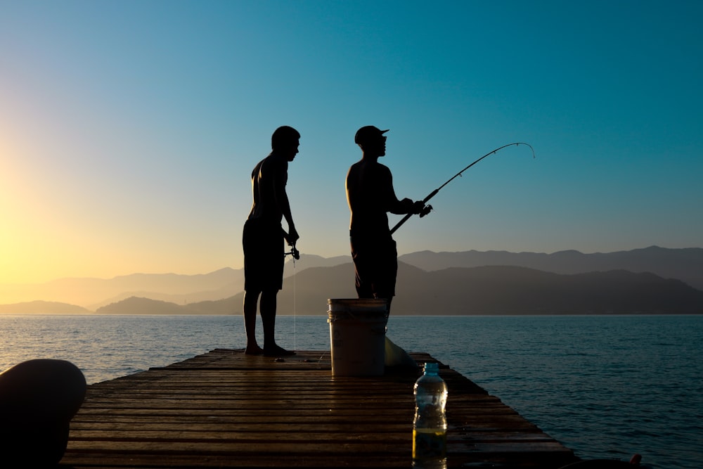 silhouette of man and woman holding fishing rod standing on dock during sunset