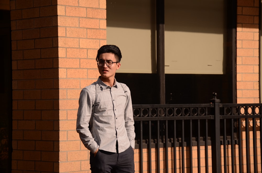 man in blue dress shirt and black pants standing near brown brick wall