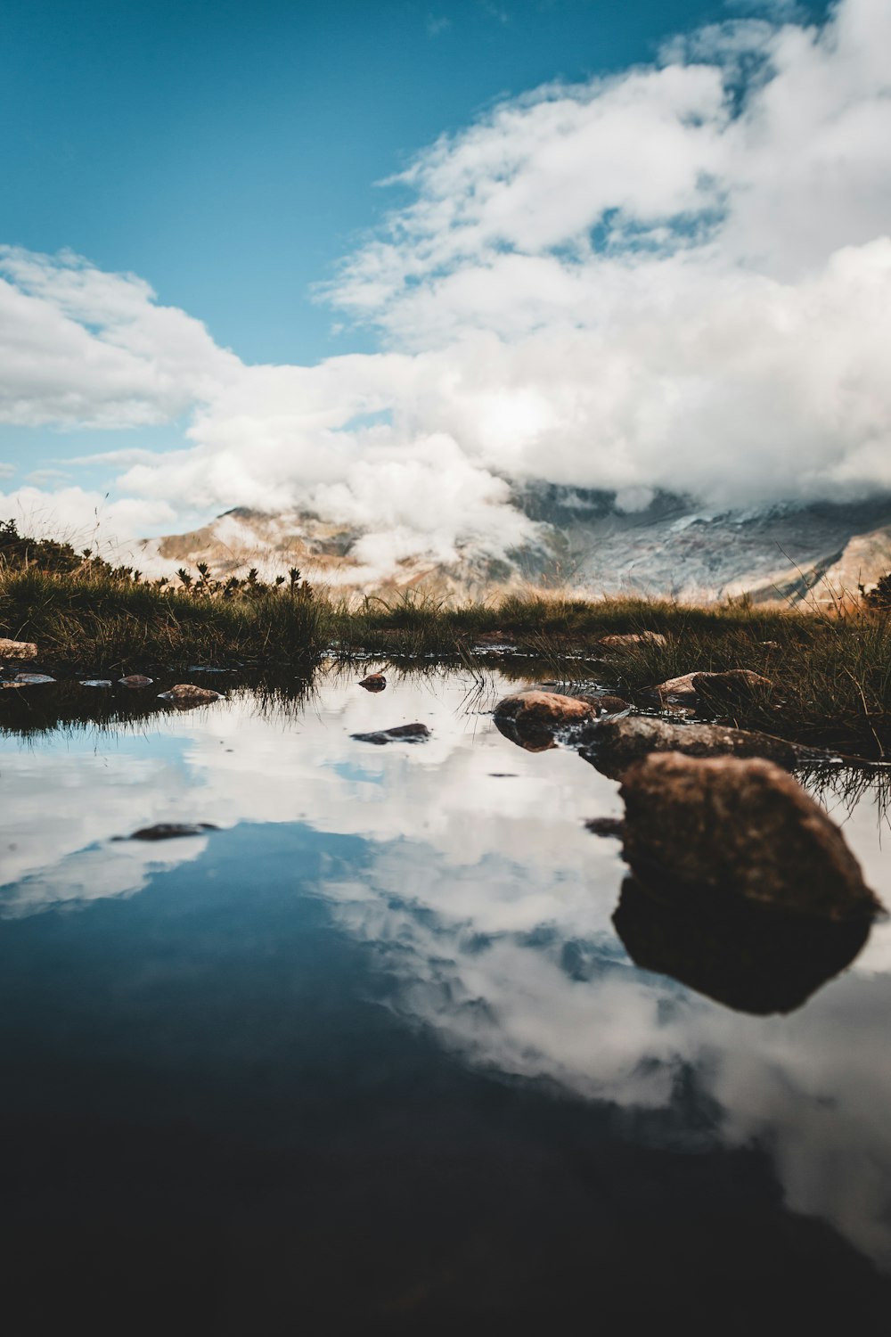 body of water near green grass under white clouds during daytime