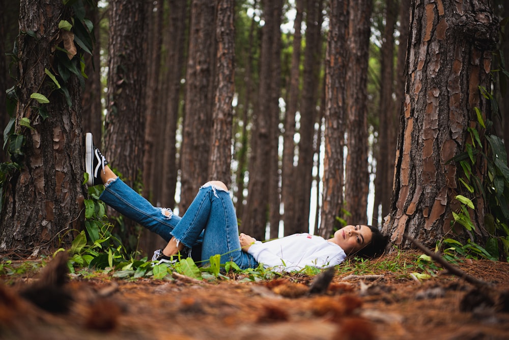 woman in white shirt and blue denim jeans lying on ground with dried leaves
