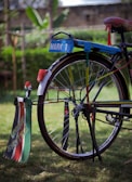 A colorful bicycle with a custom design featuring bright colors and personalized text. The back wheel has vibrant decorations and signage that reads 'Mark 1' and 'Unique Shuttle'. The bicycle stands on a grassy surface, with a blurred green natural background.