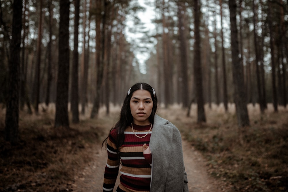 woman in gray coat standing in the woods during daytime