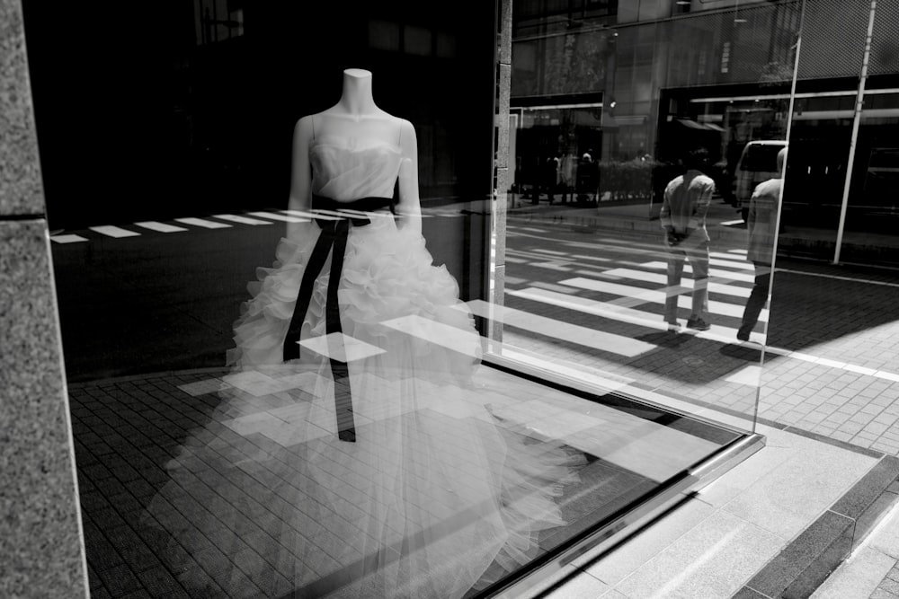 Foto in scala di grigi di donna in abito bianco in piedi sul marciapiede