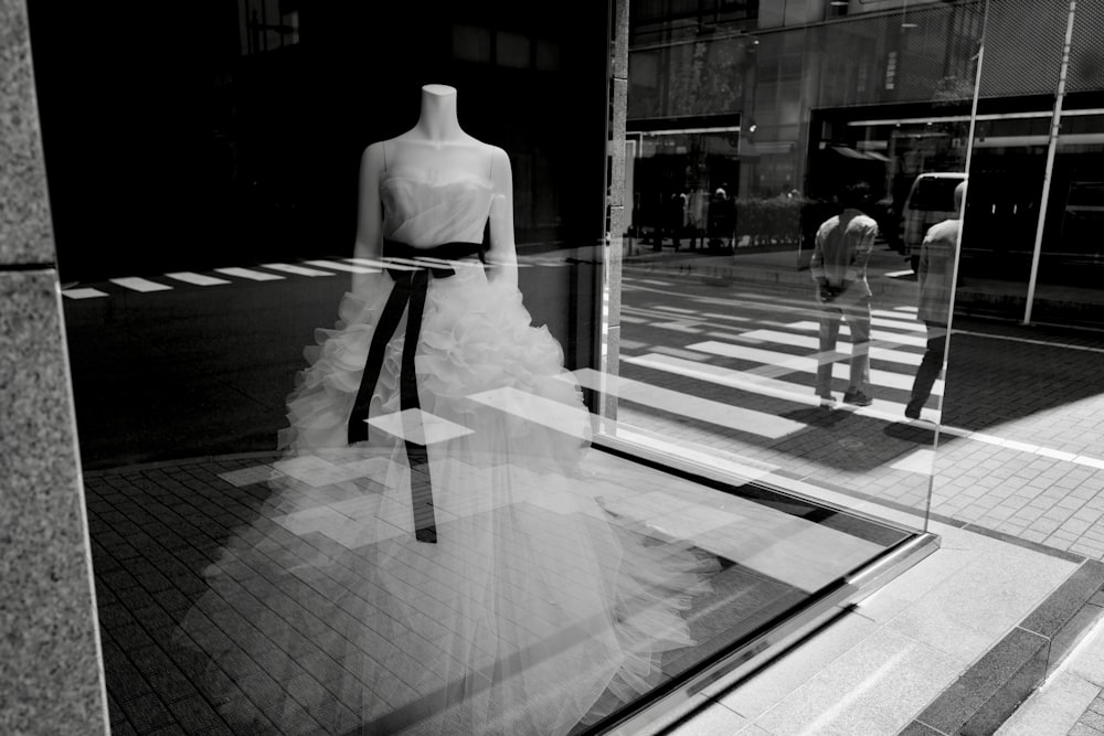 Foto en escala de grises de mujer con vestido blanco de pie en la acera