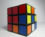 A partially solved Rubik's Cube featuring a mix of red, blue, yellow, orange, white, and black colors. The cube is positioned against a plain white background.