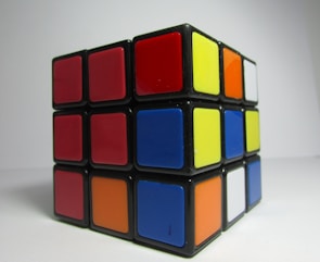 A partially solved Rubik's Cube featuring a mix of red, blue, yellow, orange, white, and black colors. The cube is positioned against a plain white background.