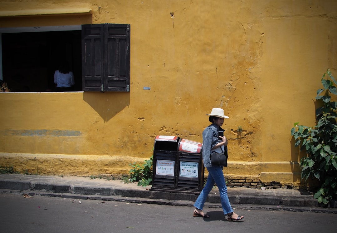 woman in blue denim jacket and blue denim jeans standing beside yellow concrete building during daytime