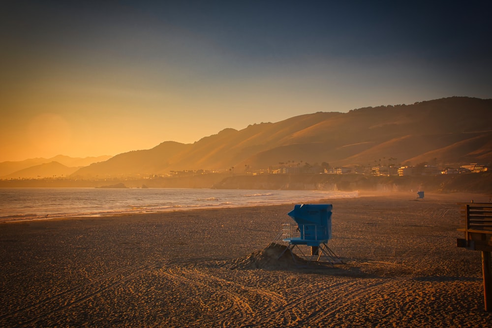 blue and white lifeguard house on beach during sunset