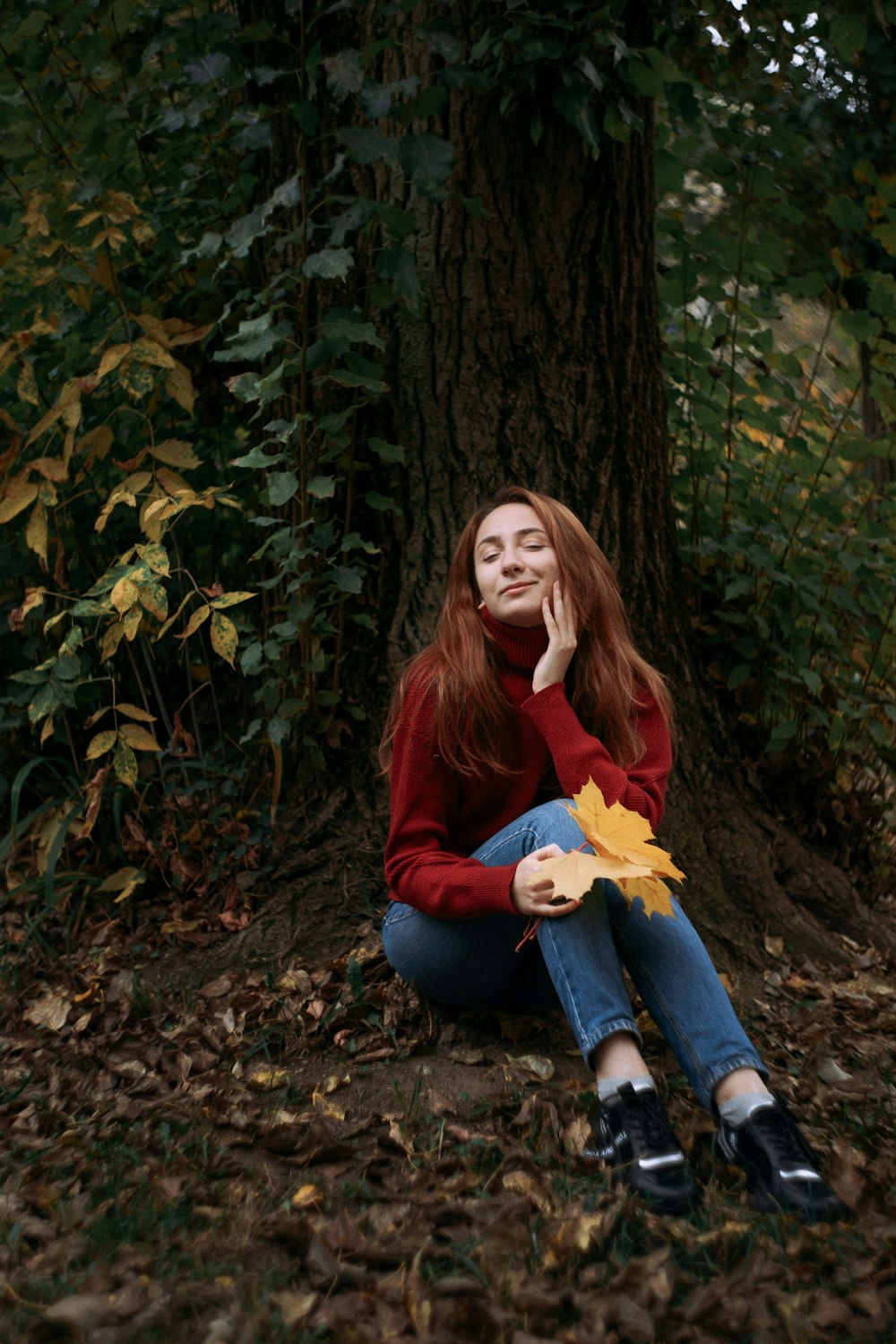 woman in red long sleeve shirt and blue denim jeans sitting on brown tree trunk
