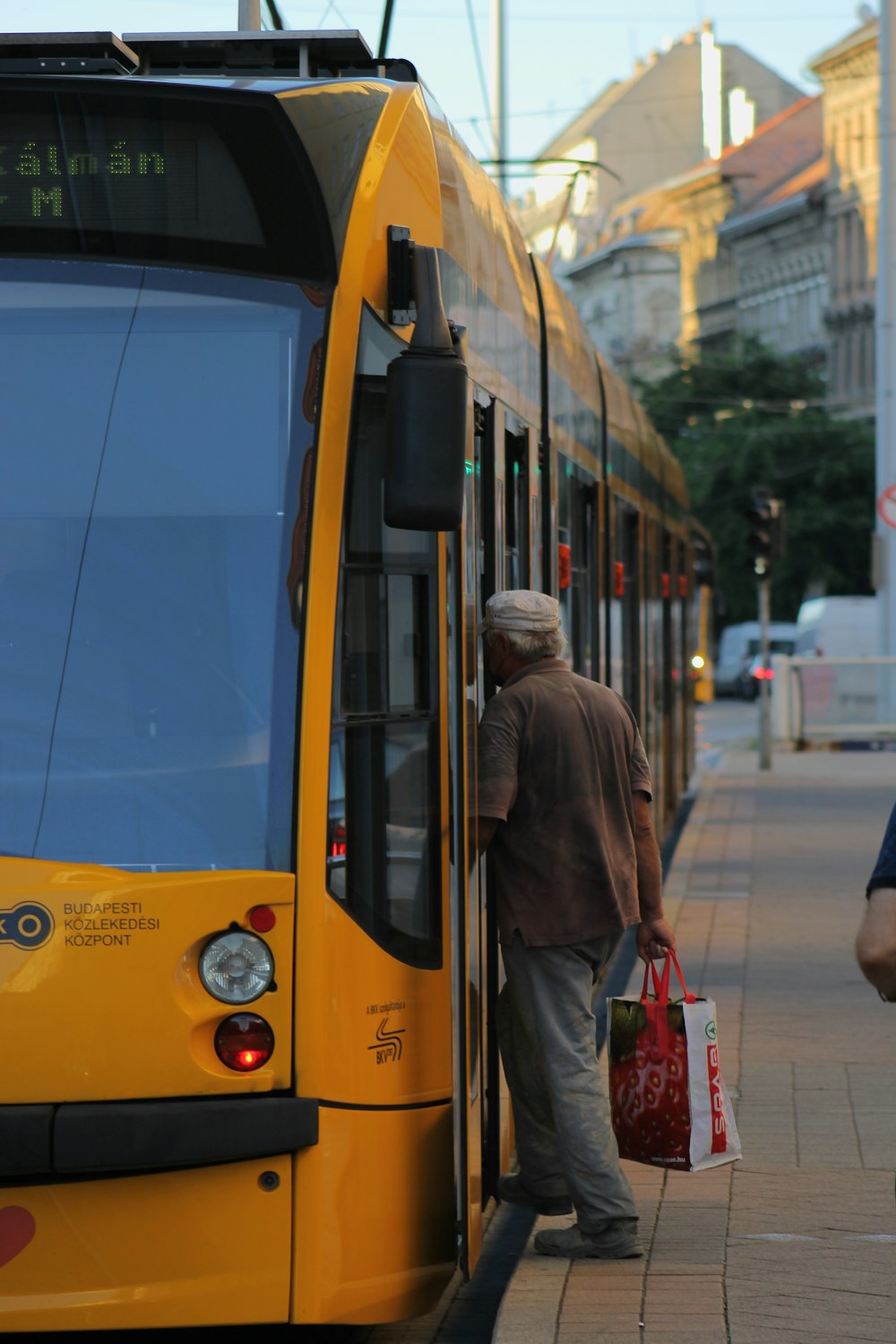 woman in brown coat standing beside yellow tram during daytime