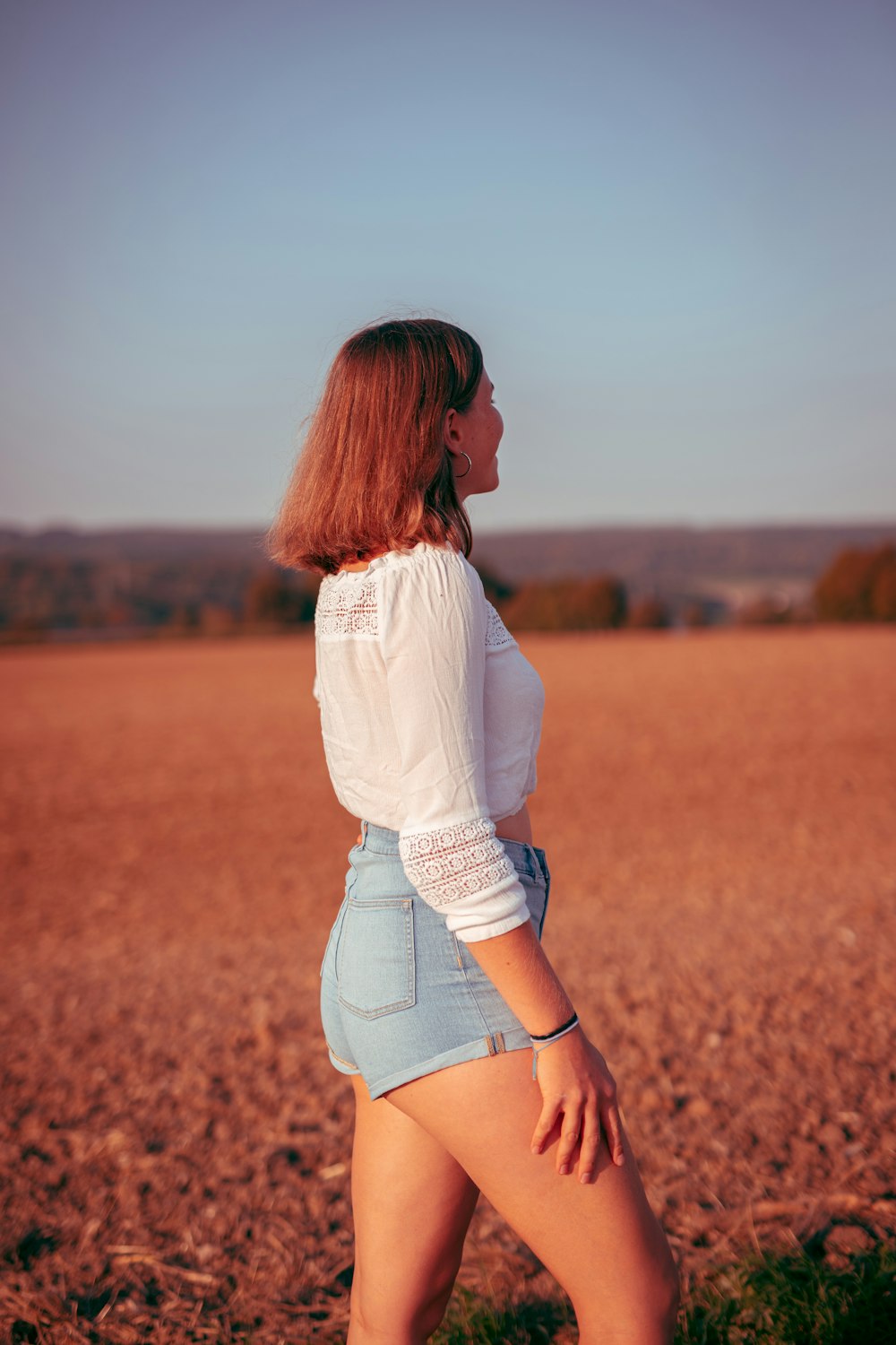 woman in white long sleeve shirt and blue denim shorts standing on brown grass field during