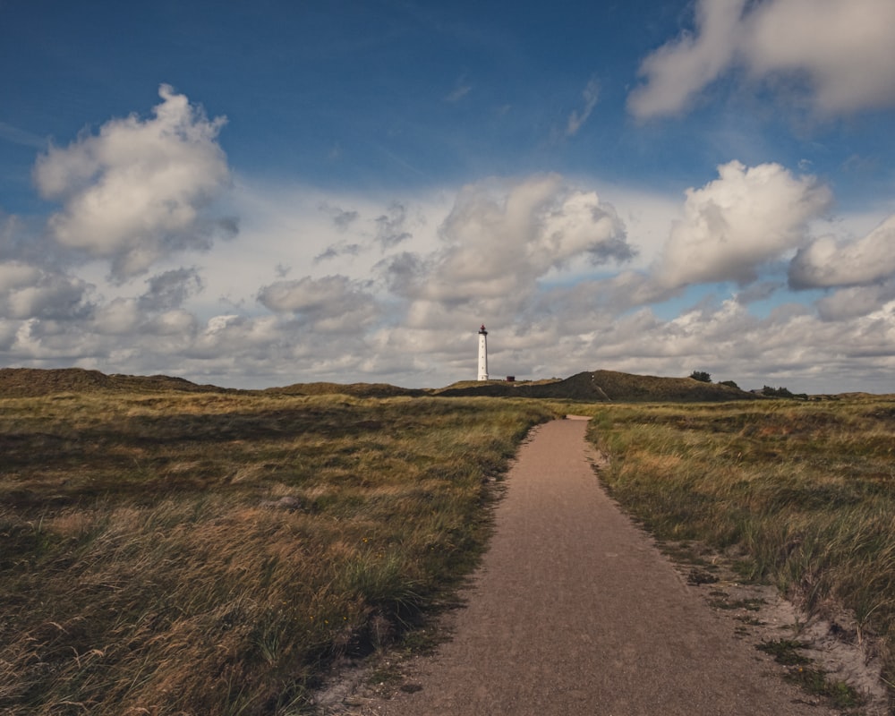 white lighthouse on green grass field under blue and white cloudy sky during daytime