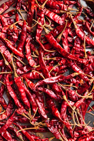 Vibrant dried red chili peppers piled in a woven basket, highlighting their rich color and texture.