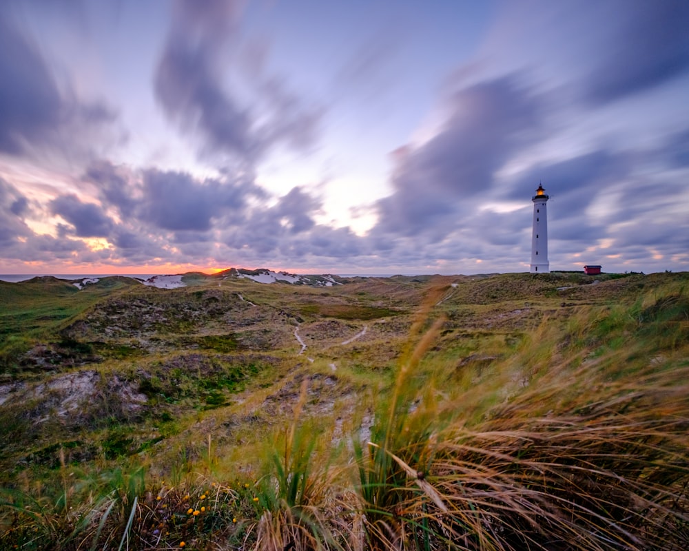 white and black lighthouse on green grass field under cloudy sky during daytime