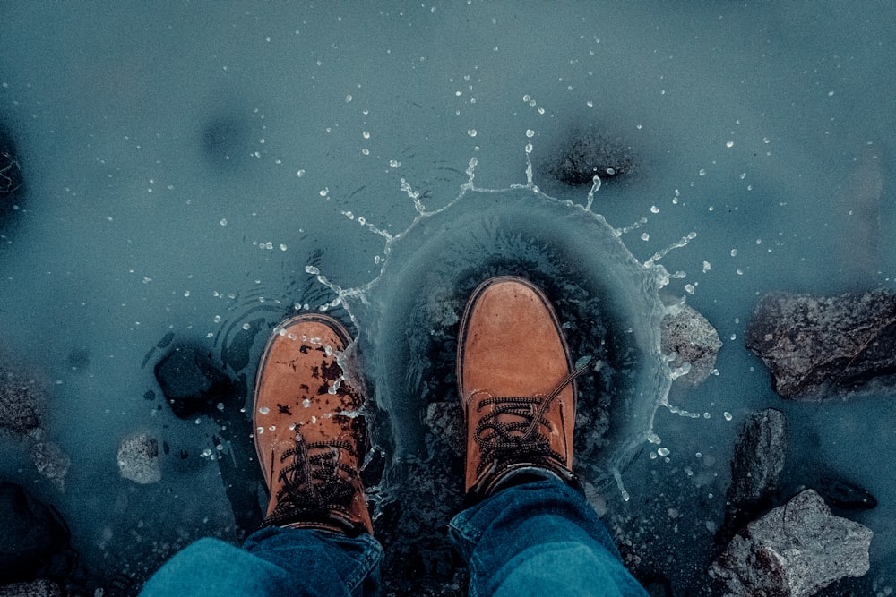 person in blue denim jeans and brown shoes standing on water