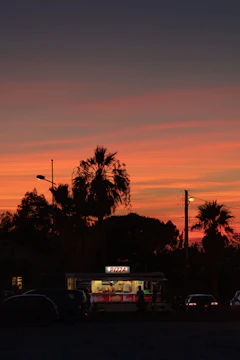 A vibrant food truck at sunset serving happy customers on a busy street.