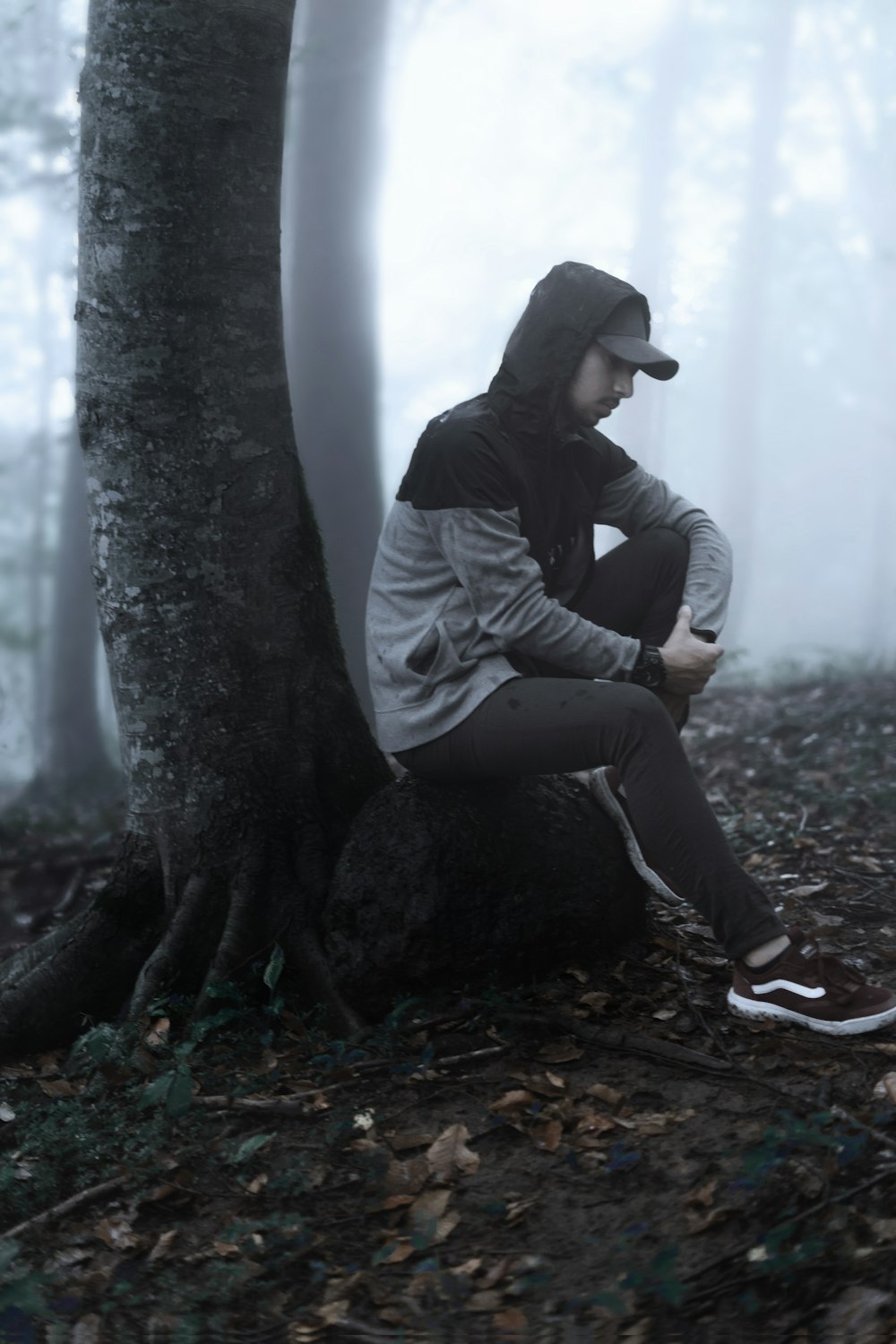 man in gray jacket and black pants sitting on tree trunk