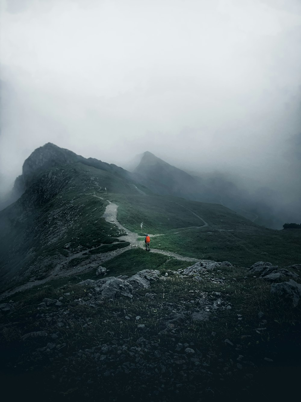 person in orange jacket standing on rock formation during foggy weather