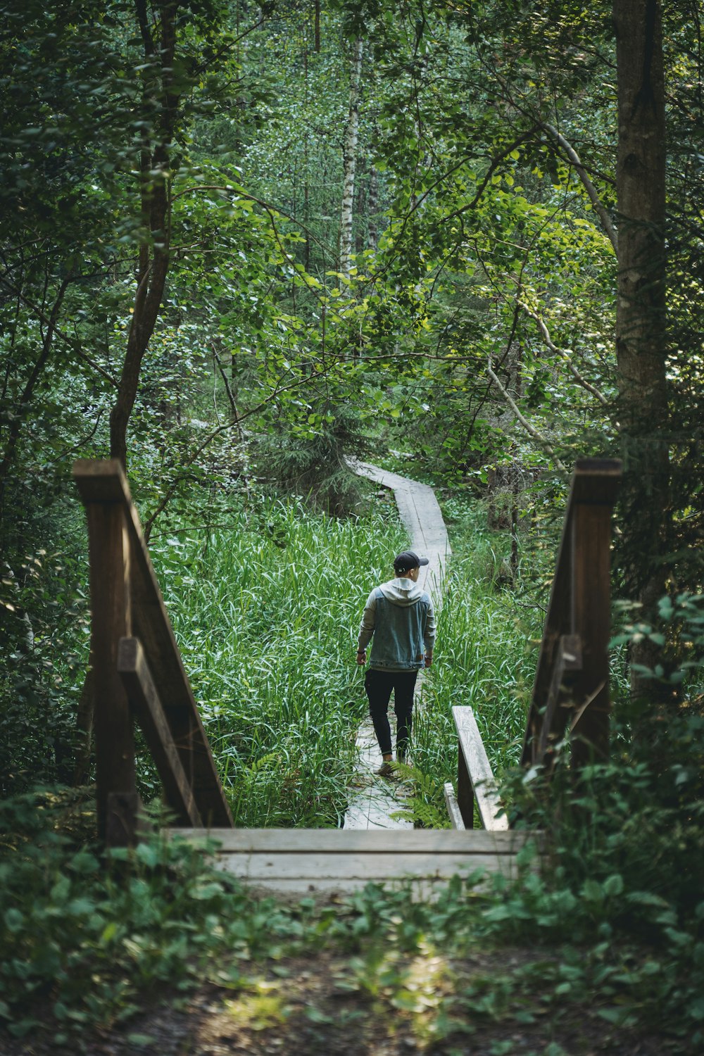 man in white shirt and black pants walking on brown wooden bridge