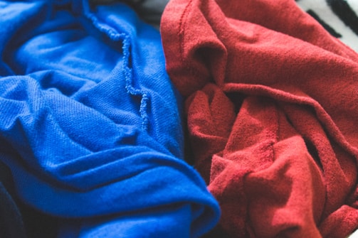 A detailed close-up view of two pieces of fabric with rich textures, one vividly blue and the other a striking red. The fabrics have a soft, woven appearance with folds and creases adding depth and complexity.