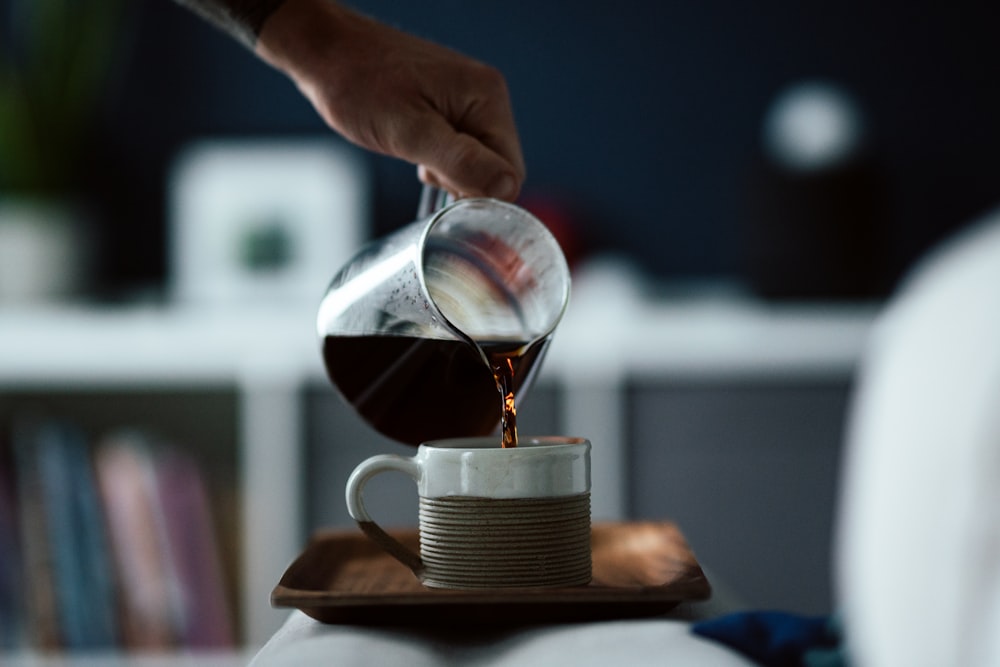 person pouring water on brown ceramic mug