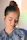 A woman with her hair styled in a bun has her eyes gently closed. She wears a light blue, patterned top, and soft, natural makeup. Sunlight creates a subtle rainbow effect near her face, adding a serene ambiance.