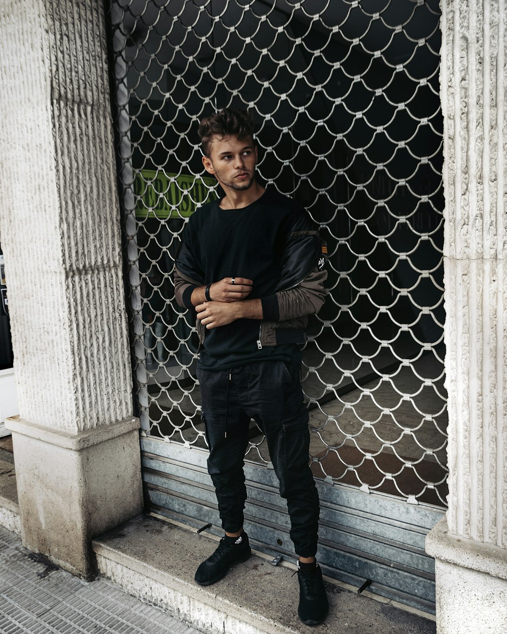 man in black crew neck t-shirt and blue denim jeans standing beside gray metal fence