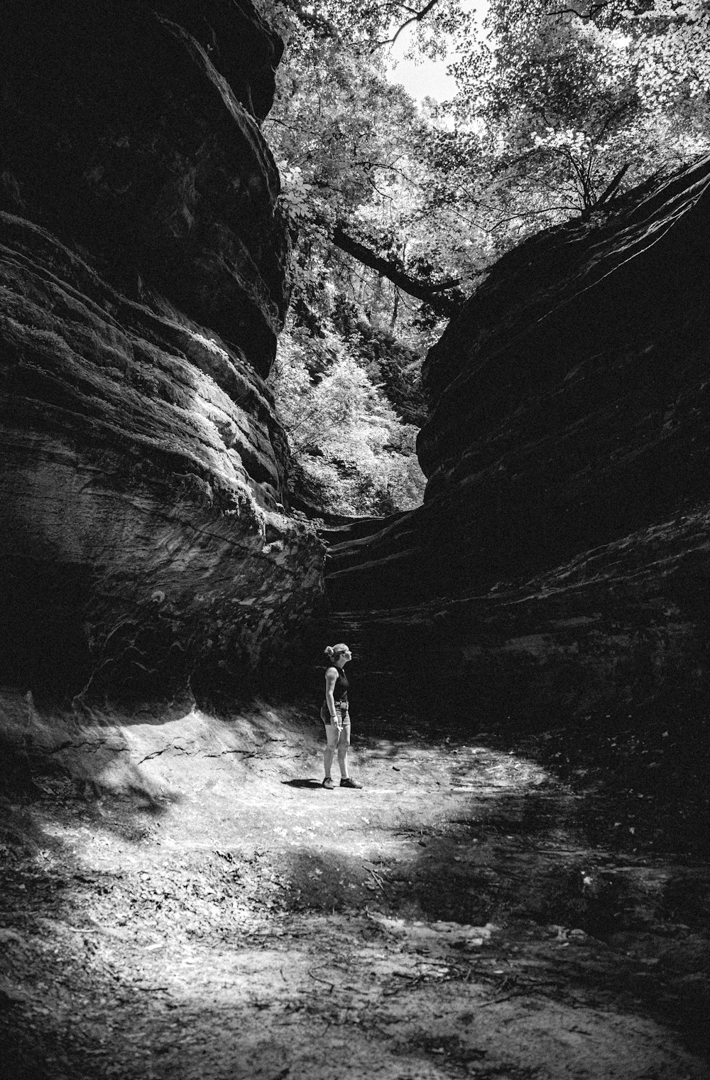 grayscale photo of man in black shorts standing in front of rock formation