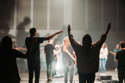 A diverse group of people raising hands in worship under warm stage lights.