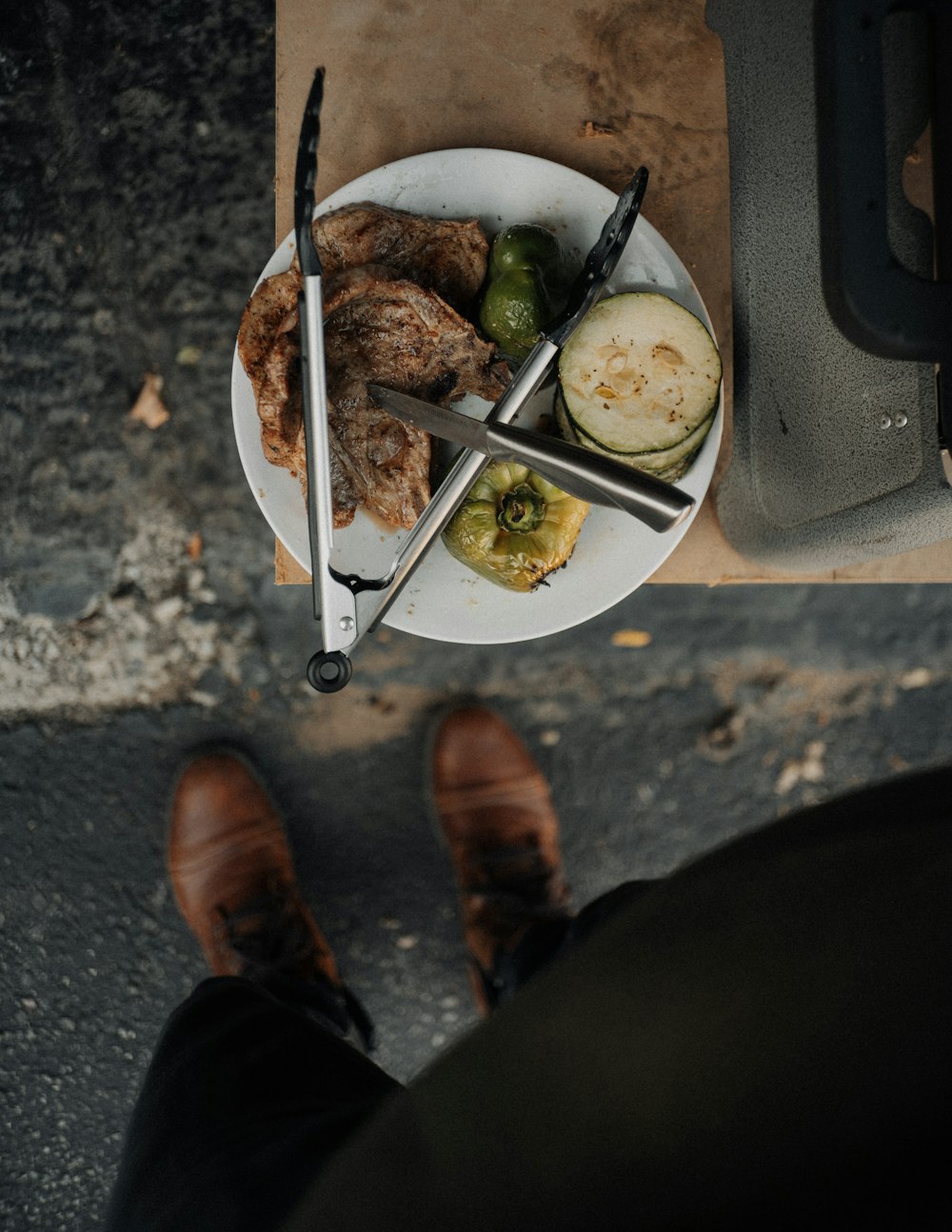 person in brown leather shoes standing in front of white ceramic plate with food