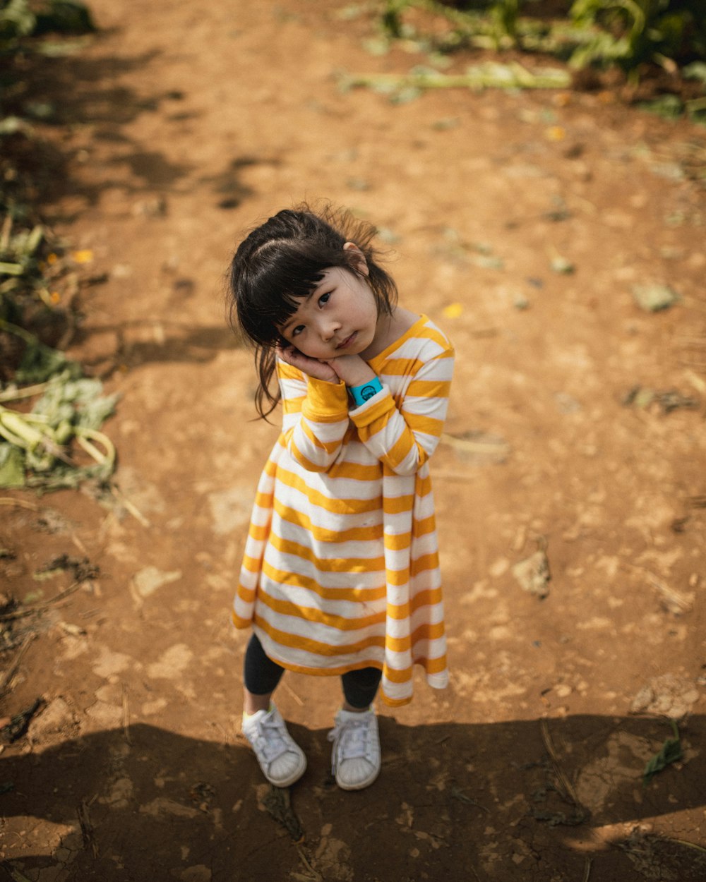 child in yellow and white striped hoodie and blue pants standing on brown soil during daytime