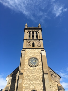 A vintage tower clock face against a bright blue sky.