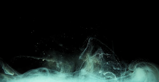 A dark background with swirling, ethereal wisps of mint green and white, resembling smoke or mist. The light streams seem to glow against the deep black, creating a mysterious and otherworldly effect.