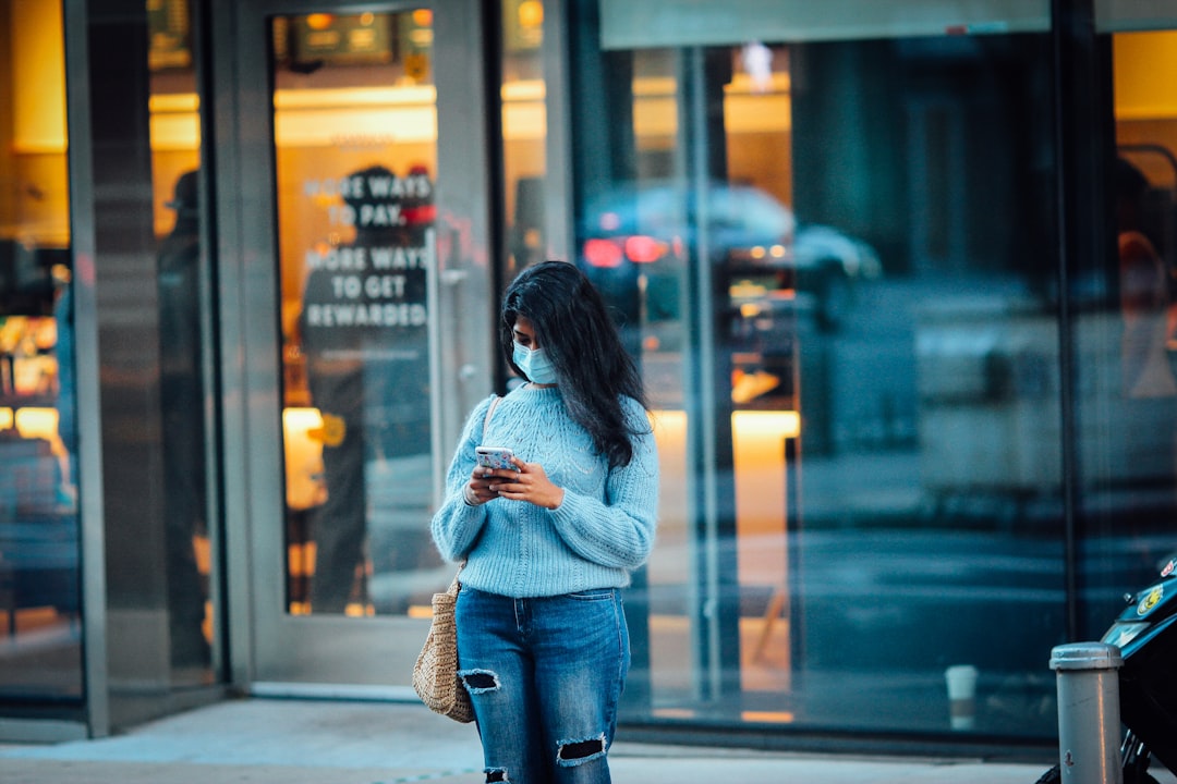 woman in gray sweater and blue denim jeans standing on sidewalk during daytime
