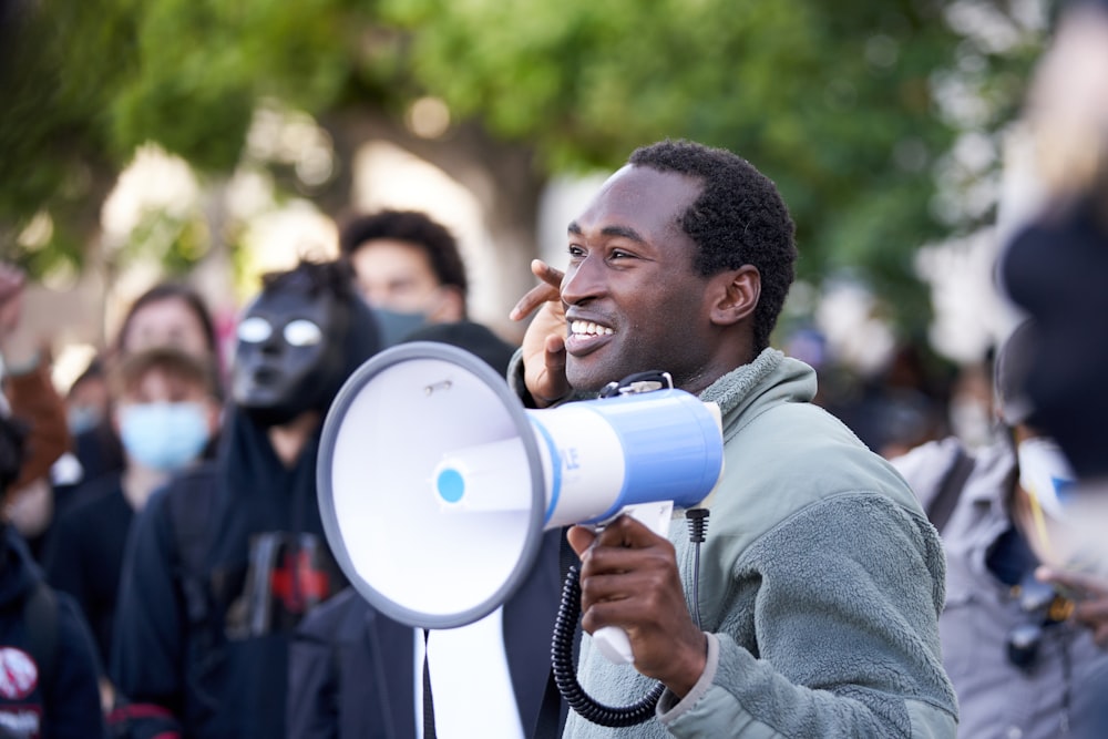 man in gray hoodie holding blue and white portable speaker