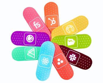 A set of colorful bandages arranged in a circular pattern. Each bandage is adorned with a different logo or symbol, suggesting a playful representation of different brands or applications. The bandages come in colors such as orange, blue, green, purple, and pink, each with a white dotted pattern.