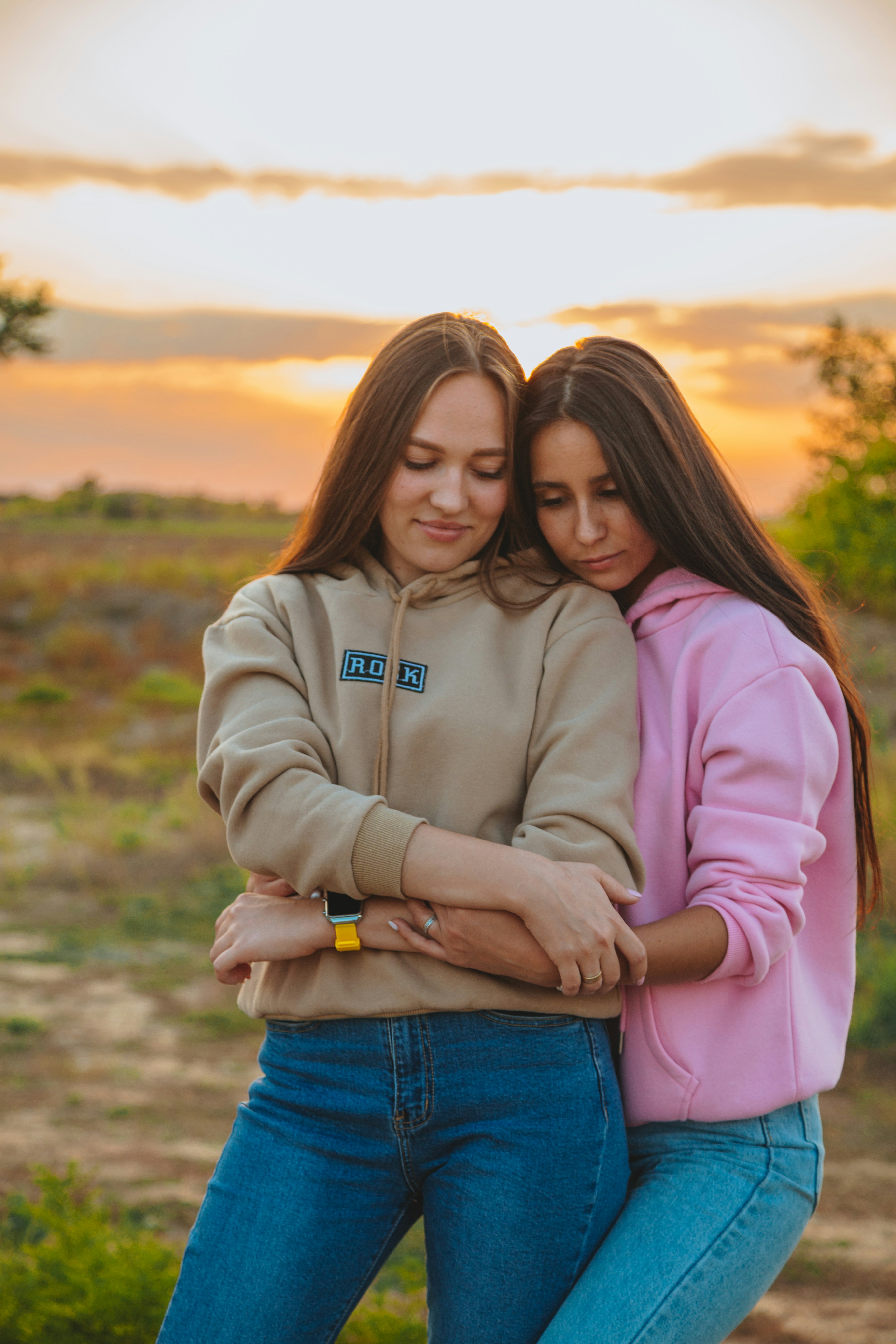 A woman in a pink hoodie standing on a brown grass field during the day