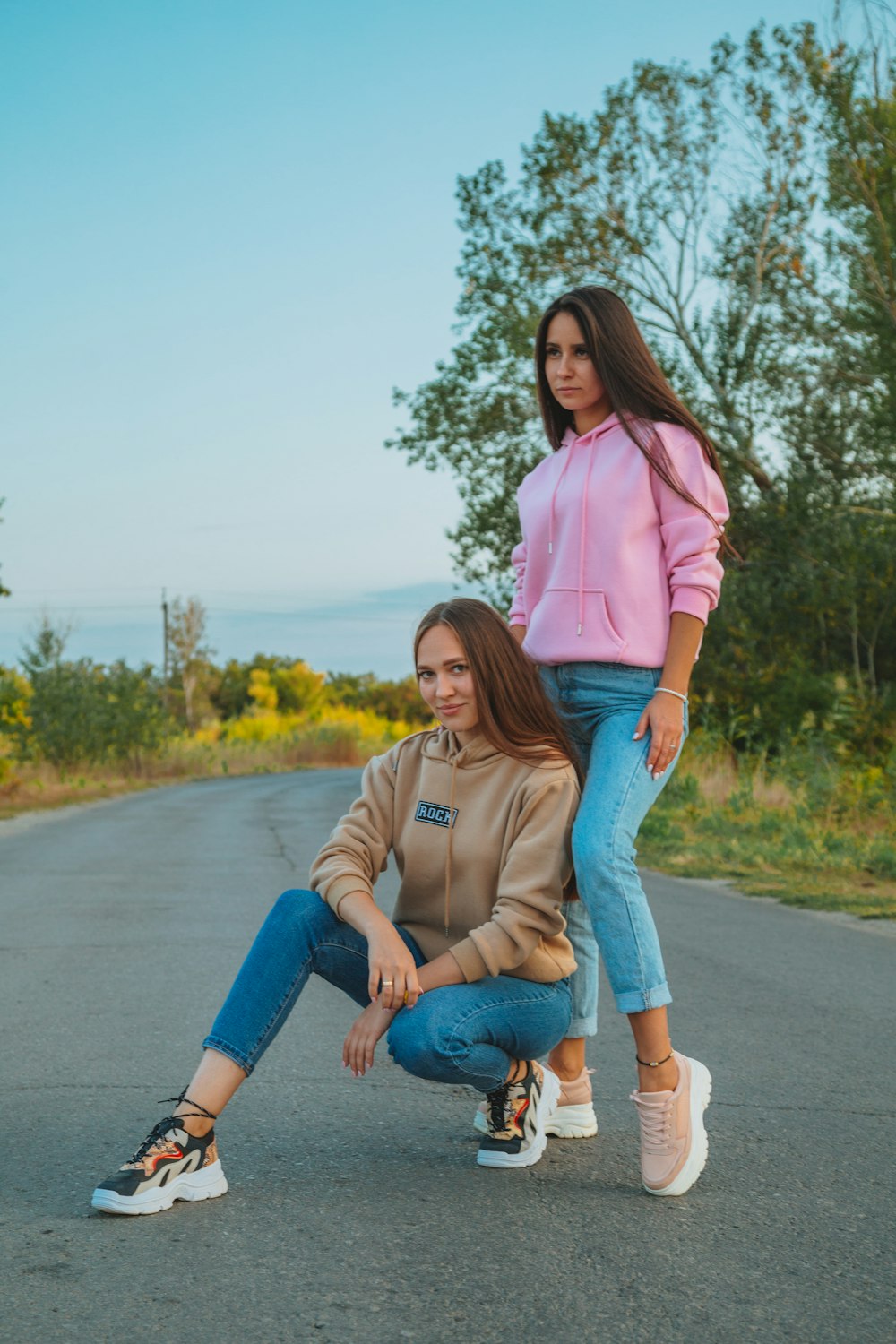 woman in pink long sleeve shirt and blue denim jeans sitting on gray asphalt road during