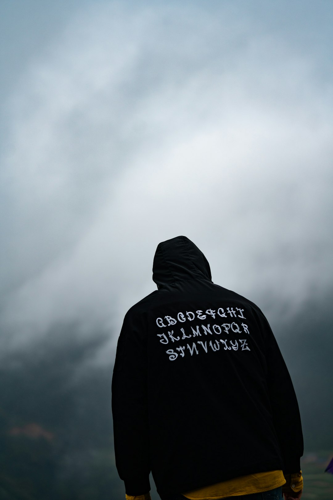 person in black hoodie standing under white clouds