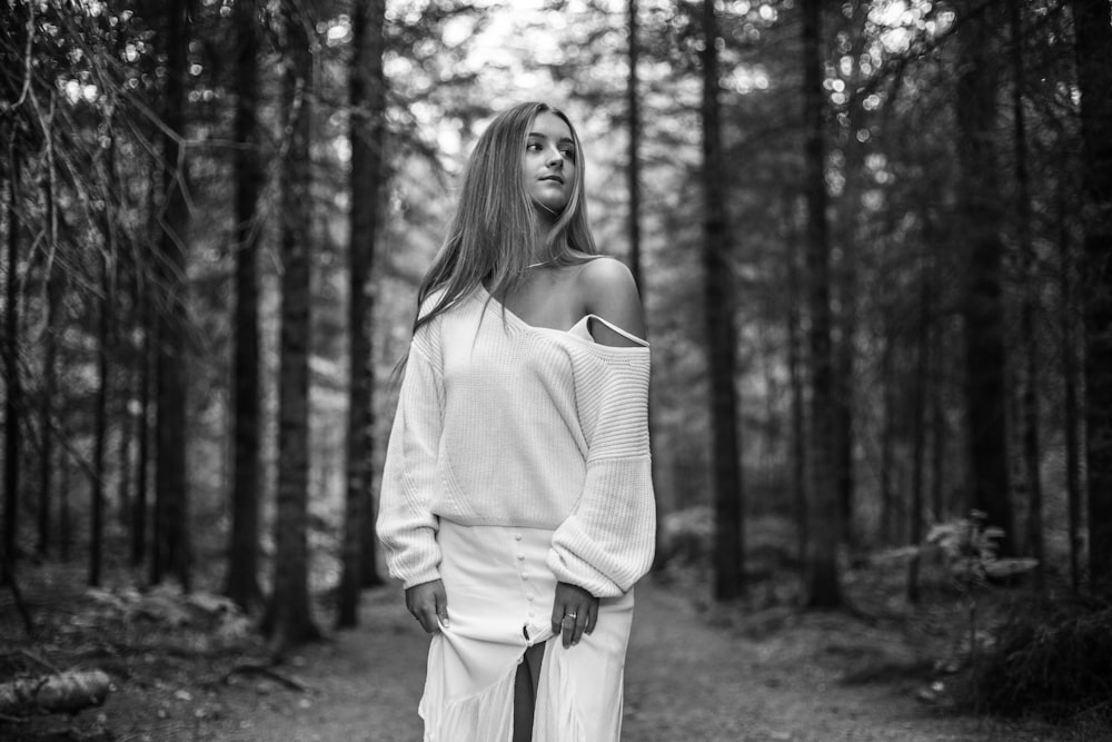 grayscale photo of woman in long sleeve shirt standing near trees