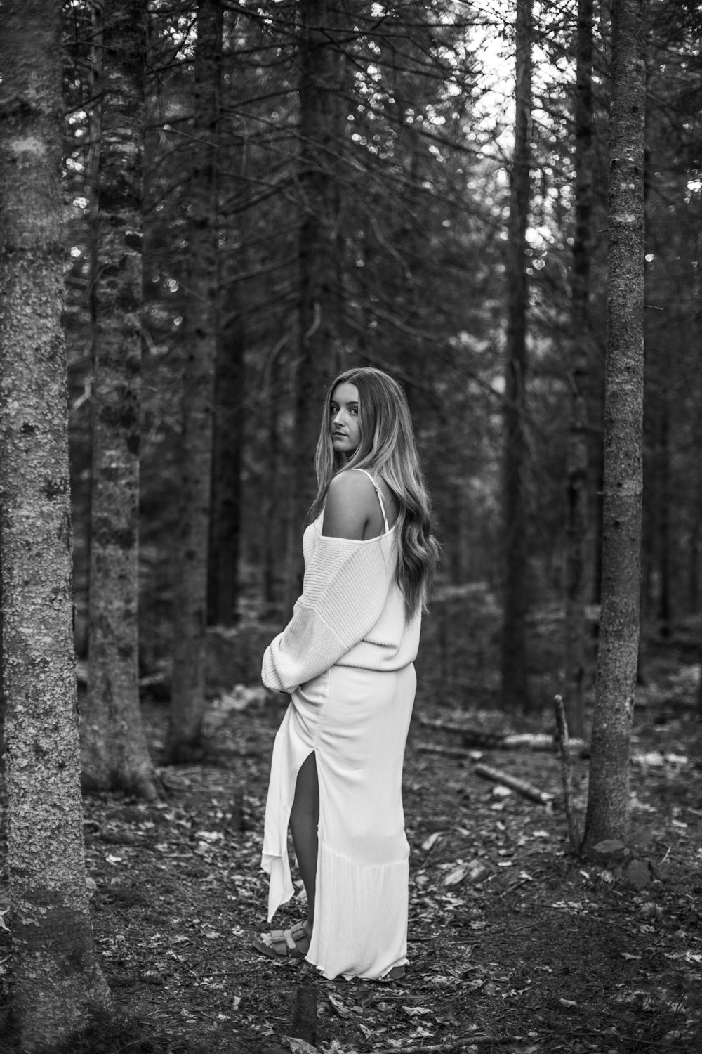grayscale photo of woman in white long sleeve shirt and pants standing near trees